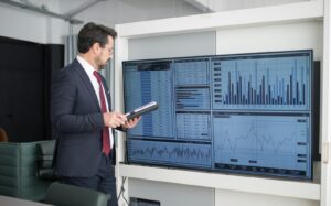 A person is looking at the monitor with numbers and graphs while presenting in an executive leadership meeting
