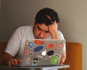A young man frustratingly looking at a laptop screen